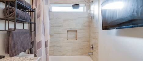A bathroom with a bathtub, a shower, a toilet, a towel rack with towels, and a mounted television.