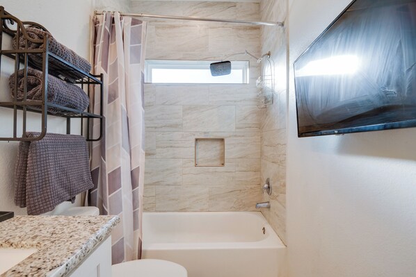 A bathroom with a bathtub, a shower, a toilet, a towel rack with towels, and a mounted television. - 2 Mi to Lake Conroe! Game-ready Group Retreat (Montgomery)