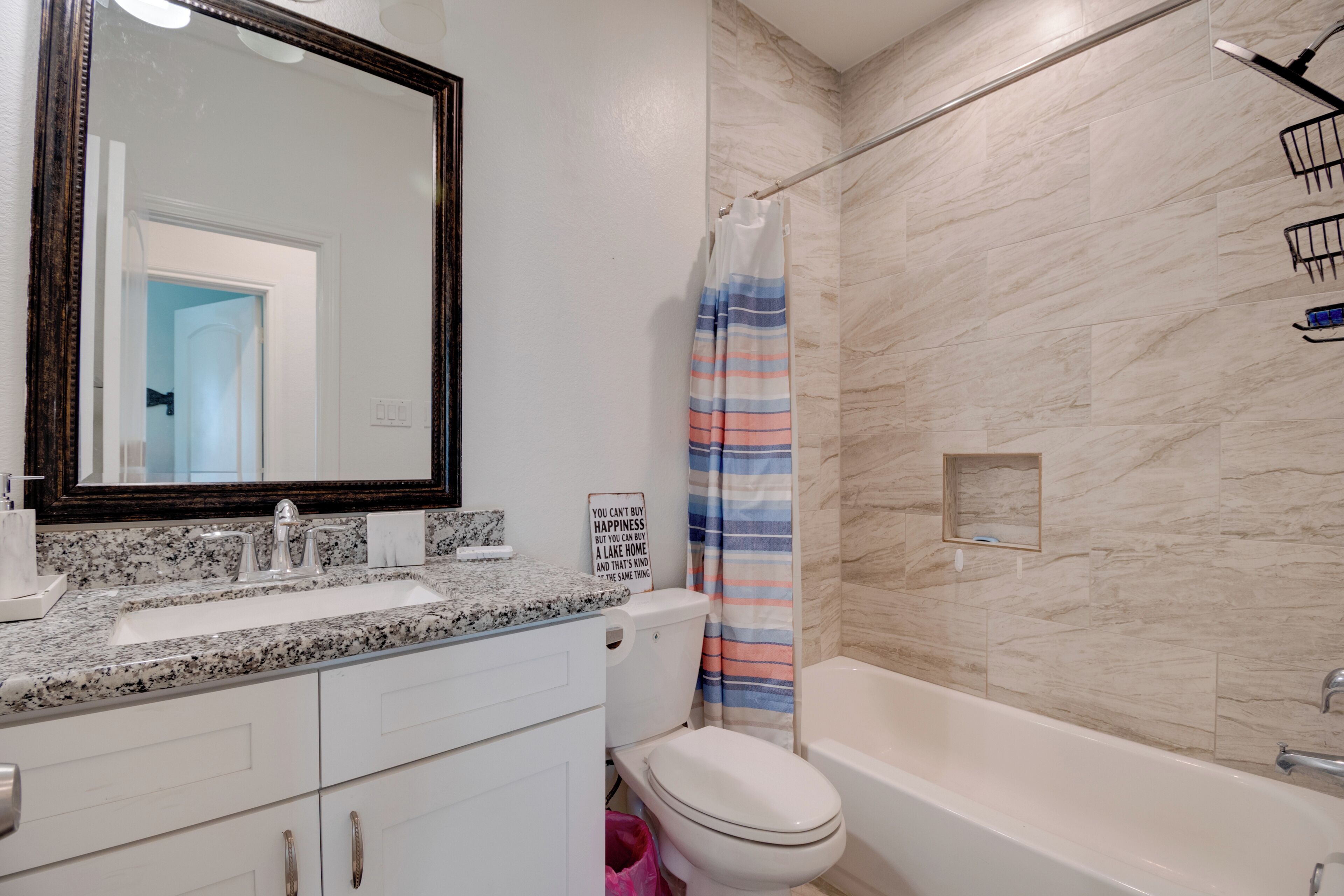 A bathroom with a granite countertop sink, a white toilet, a bathtub, and a shower curtain.