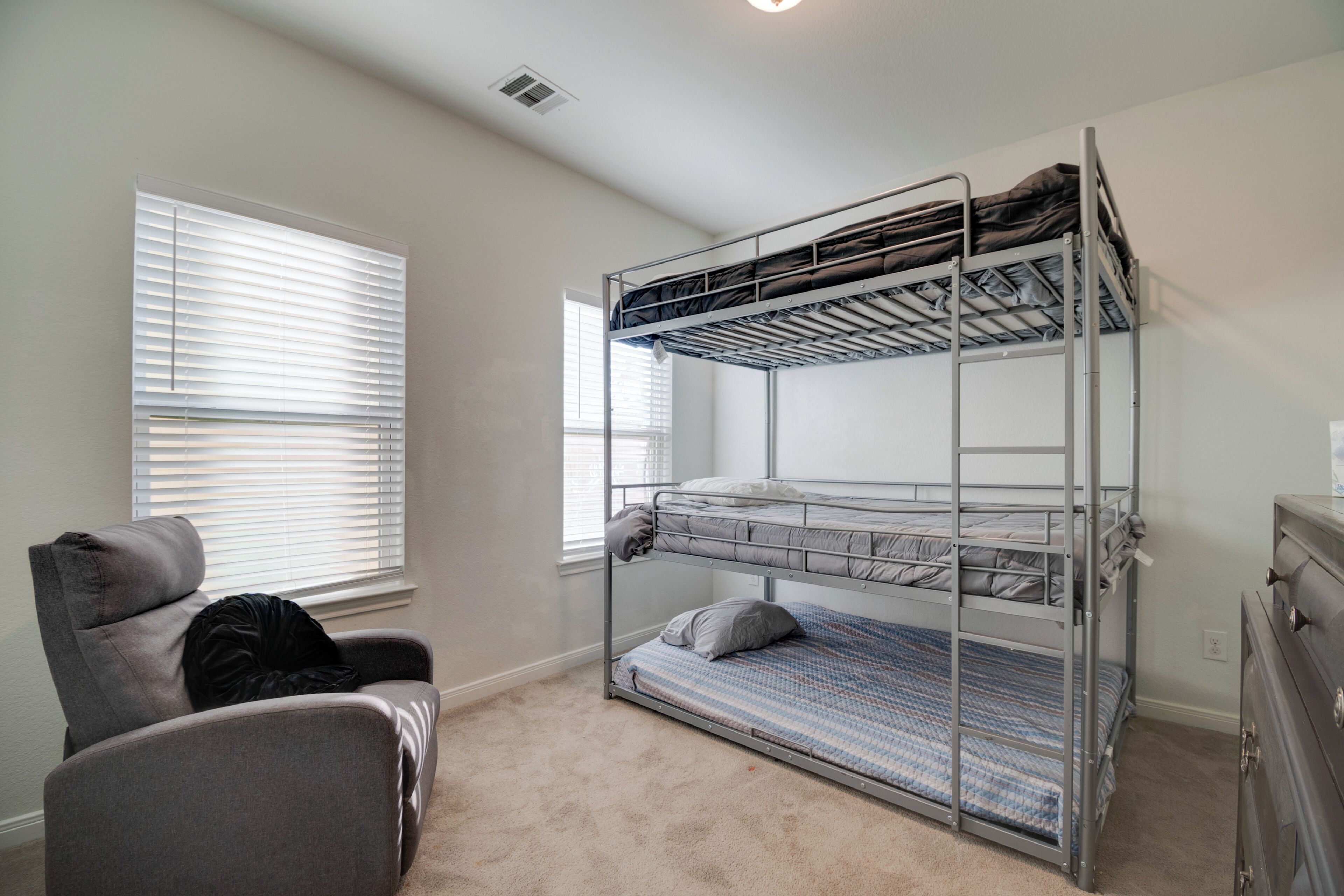 A bunk bed in a room with a window, a chair, and a dresser.