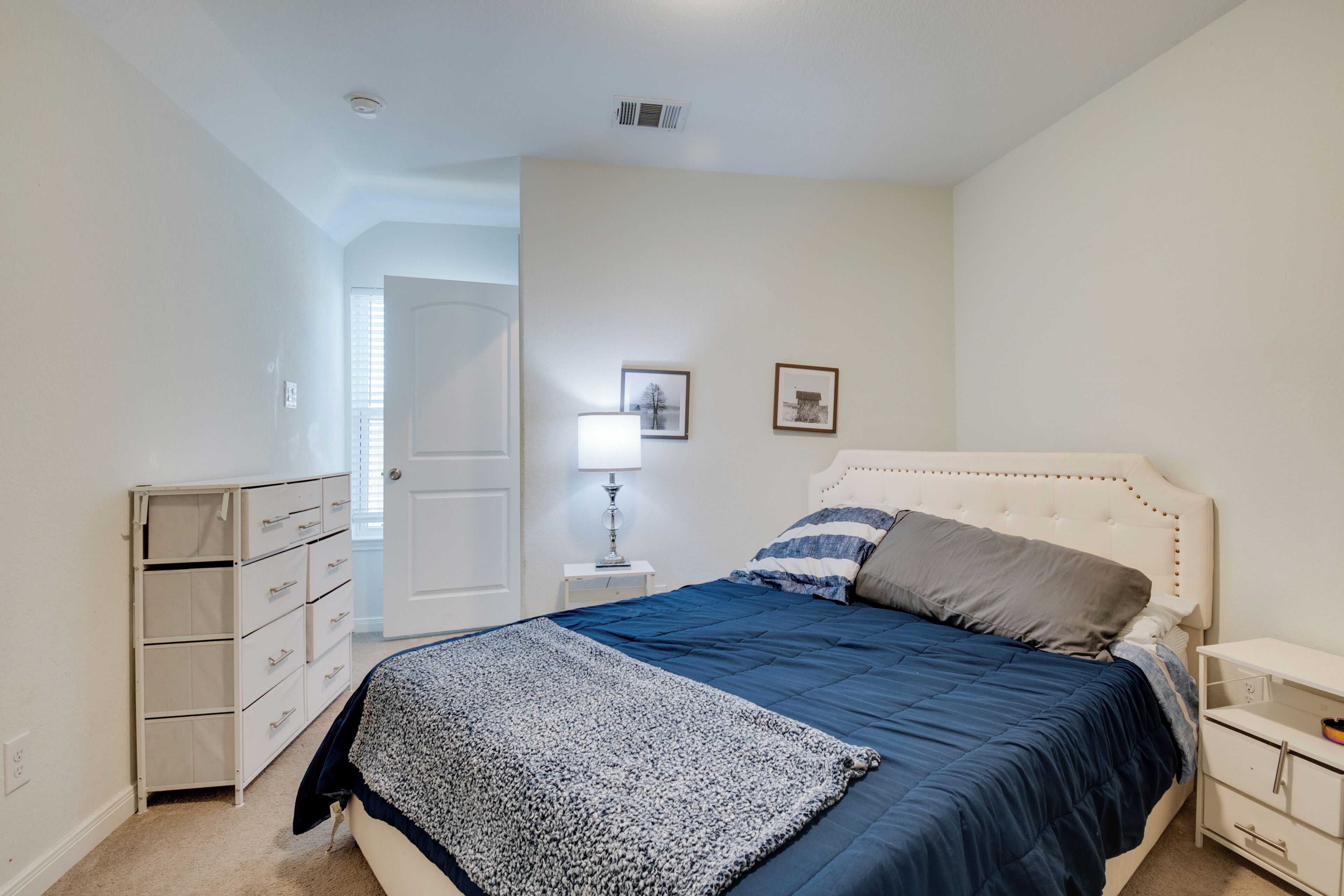 A bedroom with a bed, a nightstand, a dresser, and a door leading to another room.