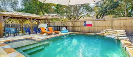 A backyard with a swimming pool, lounge chairs, and a covered patio area.