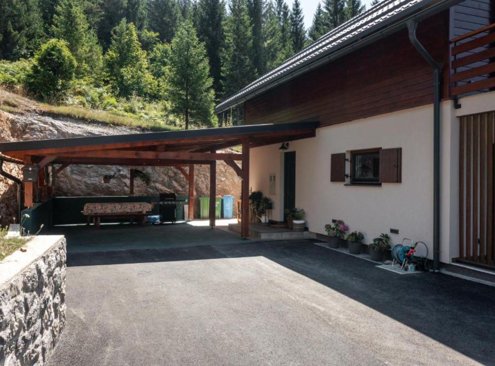 A covered outdoor area with a bench, a barbecue grill, and a stone wall.