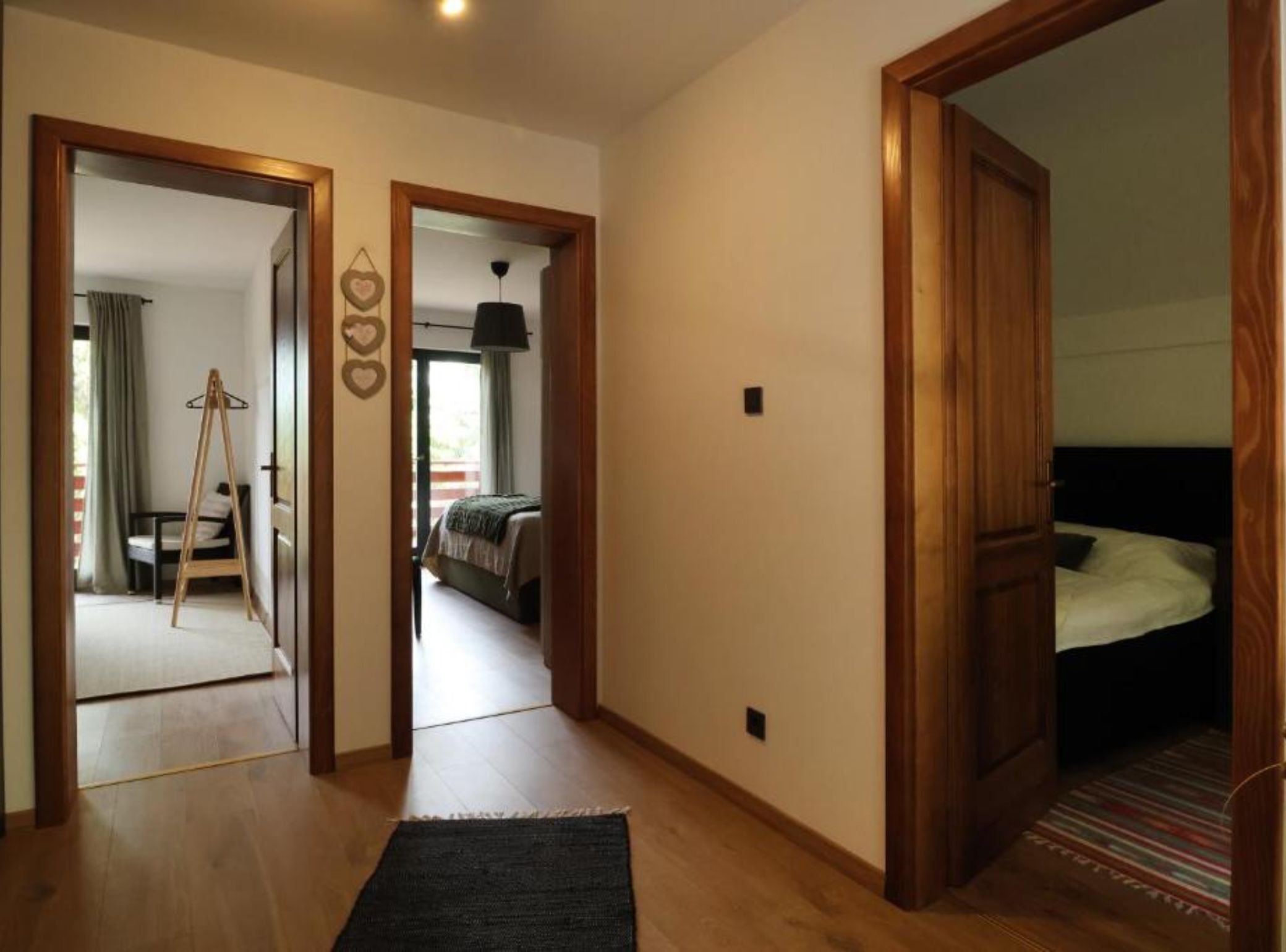 A hotel room with a wooden floor, a bed with white bedding, a black headboard, and a striped rug. There is a wooden door leading to another room.