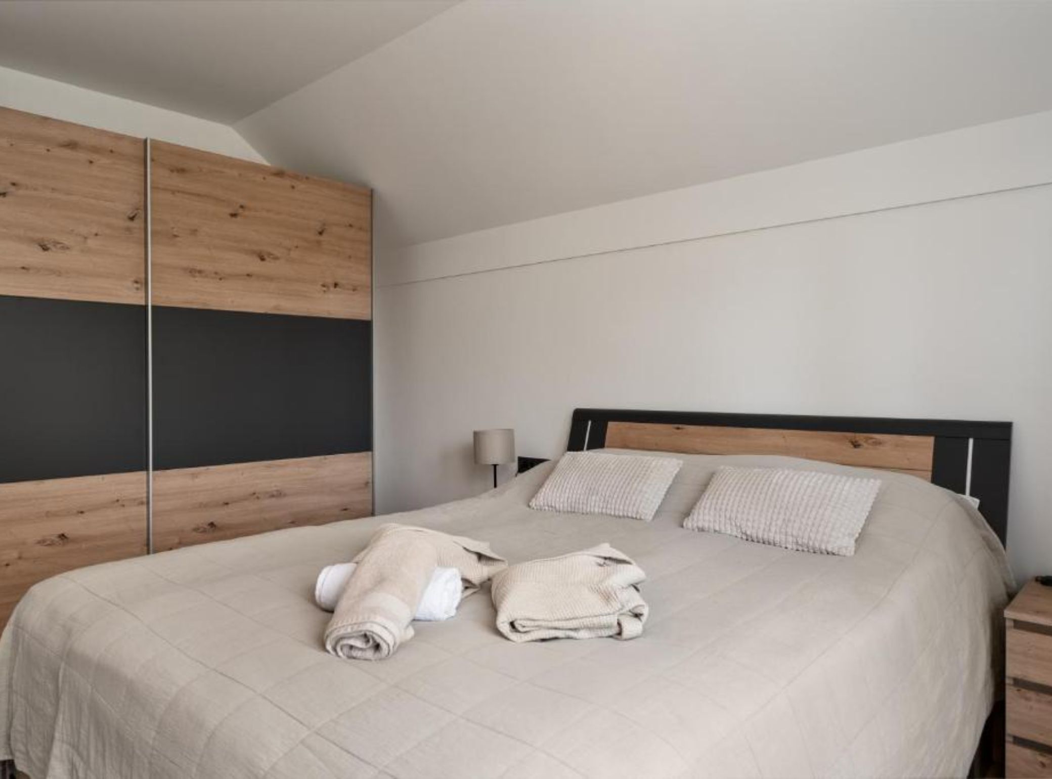 A modern bedroom with a bed, wooden wardrobe, and a nightstand.