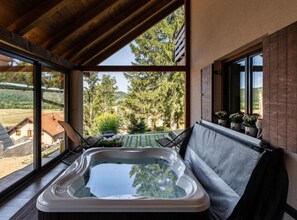 Un jacuzzi en un área exterior techada con vista a un jardín y una casa al fondo.