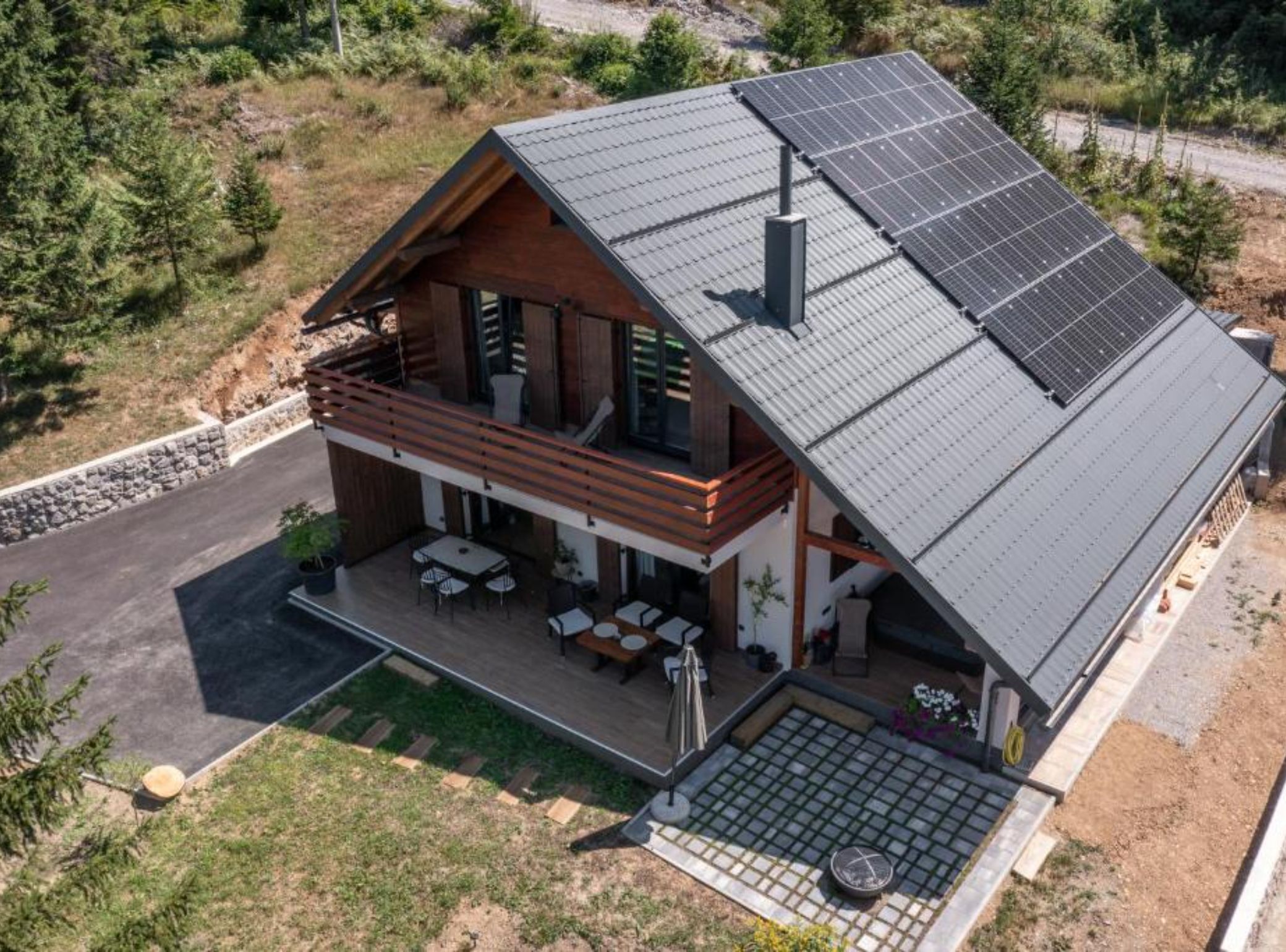Una casa moderna de dos pisos con techo inclinado, paneles solares, un balcón y un patio con mobiliario exterior.