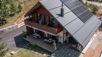 Una casa moderna de dos pisos con techo inclinado, paneles solares, un balcón y un patio con mobiliario exterior.