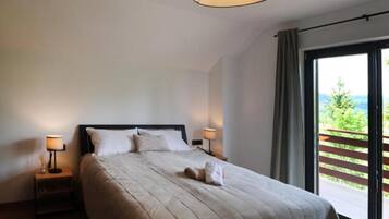 A bedroom with a large bed, two bedside lamps, a view of greenery through a balcony door.