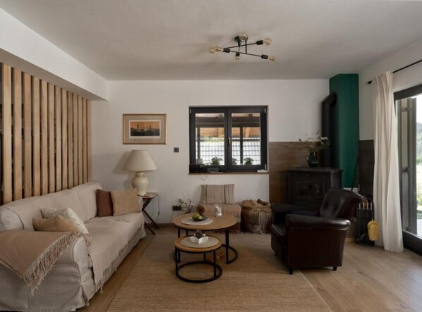 Una sala de estar con sofá, mesa de centro, silla, lámpara, chimenea y ventana con vistas.