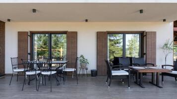 Un patio exterior con una mesa y sillas de comedor, ventanas amplias y vistas a árboles.