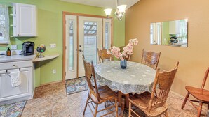 A dining area with a round table, chairs, a vase with flowers, a chandelier, and a kitchen area with cabinets and a coffee maker. - 8 Mi to Bonners Ferry: Quiet Getaway w/ Patio (Moyie Springs)