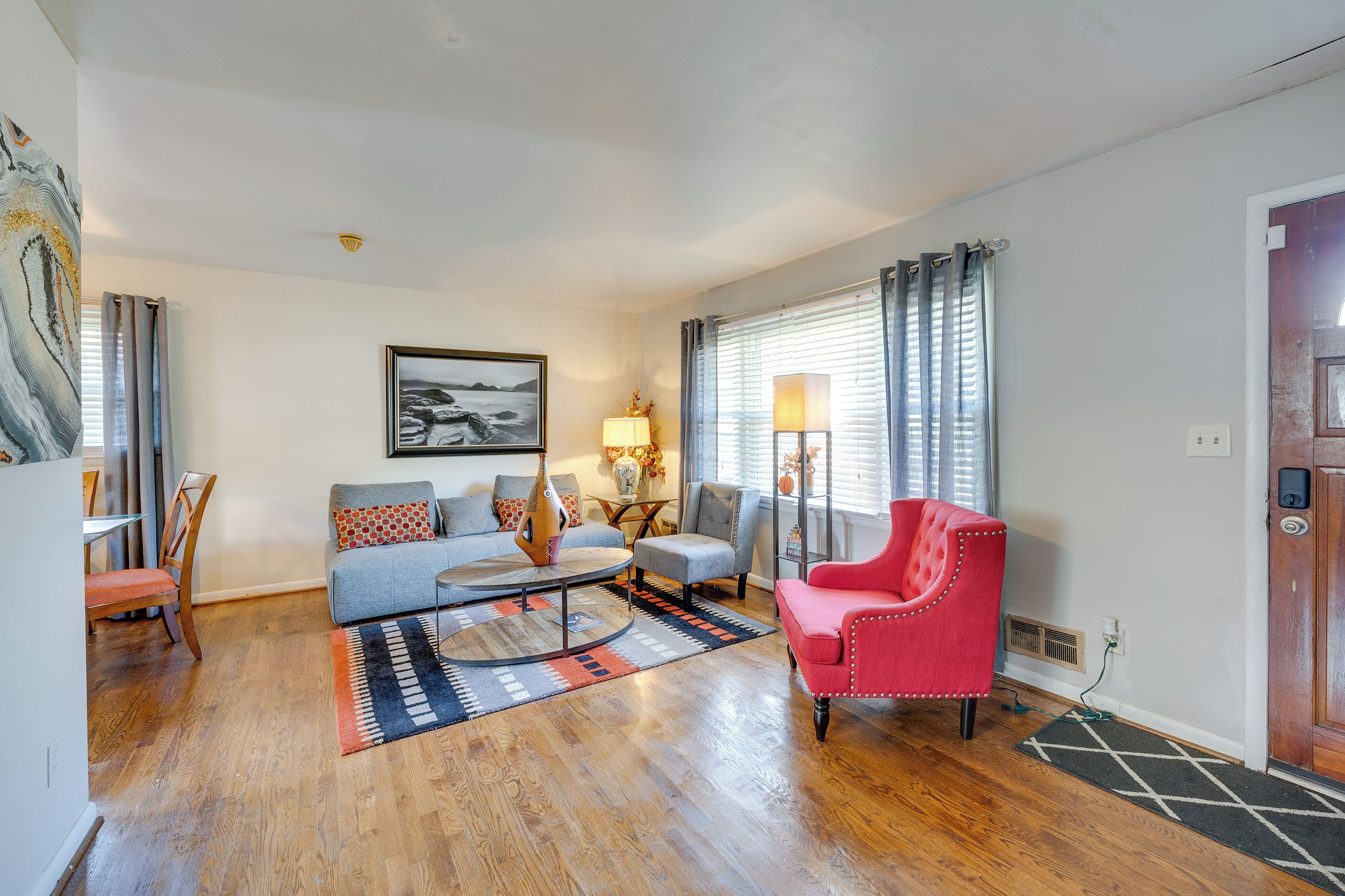 A living room with hardwood flooring, a grey sofa, a red armchair, and a coffee table.