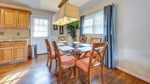 Un coin repas avec une table en verre, des chaises en bois, un luminaire suspendu et une plante en pot.