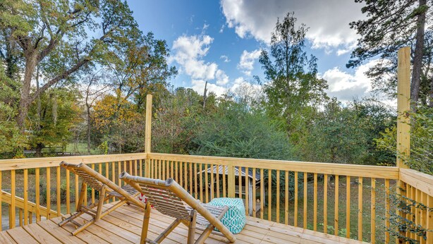 Une terrasse en bois avec une chaise en bambou et un pouf à motifs, entourée d’arbres et sous un ciel dégagé.