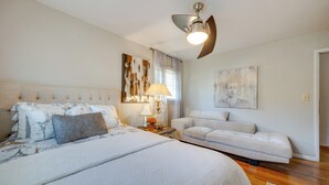 Une chambre à coucher comprenant un lit, un canapé, un ventilateur de plafond et des œuvres d’art accrochées aux murs.