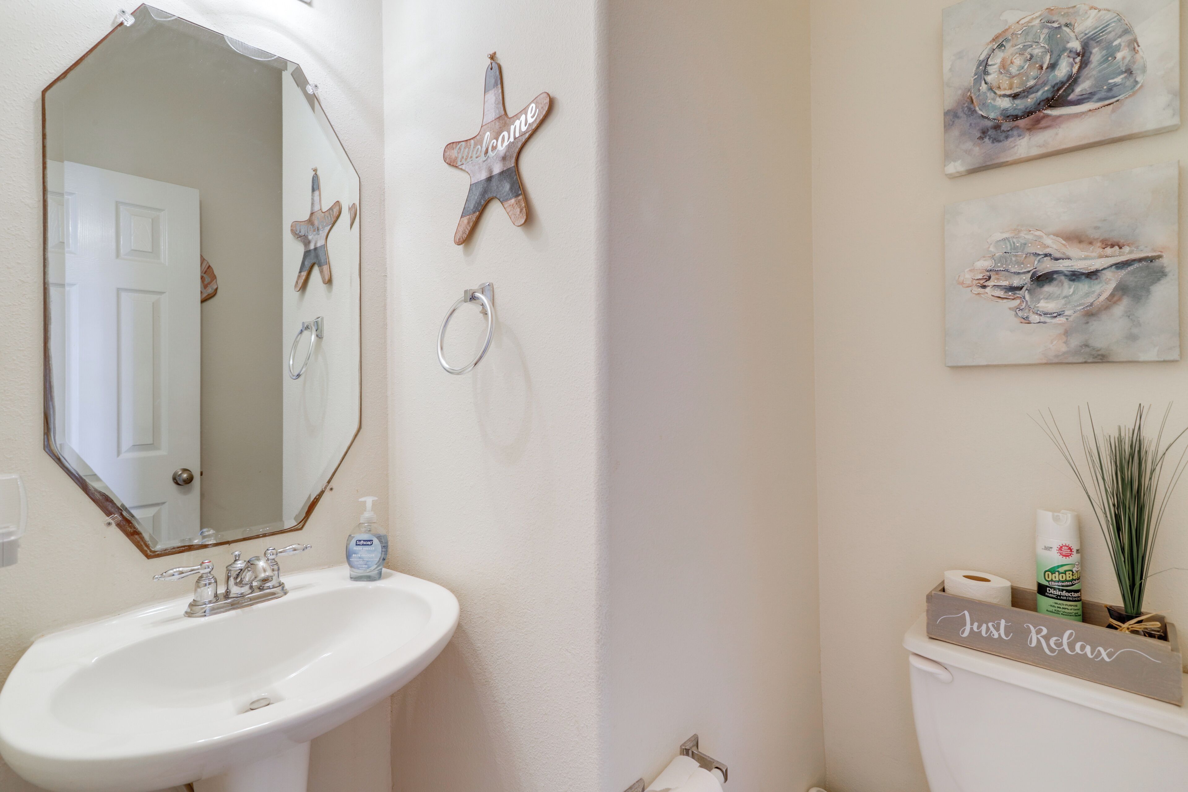Un baño con un lavamanos blanco, un espejo grande, un inodoro y decoración de estrellas de mar en las paredes.