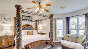 A four-poster bed with a wooden frame and a ceiling fan, a sofa with cushions, and a nightstand with a lamp. - Lake-view Home w/ Pool Access in Legends Ranch! (Spring)