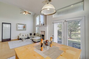Ein modernes Wohnzimmer mit Kamin, einem Esstisch mit Blumenvase und Deckenventilator.