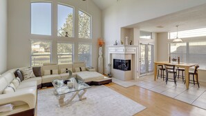A spacious living room with a fireplace, a dining area, and large windows. - Lake-view Home w/ Pool Access in Legends Ranch! (Spring)
