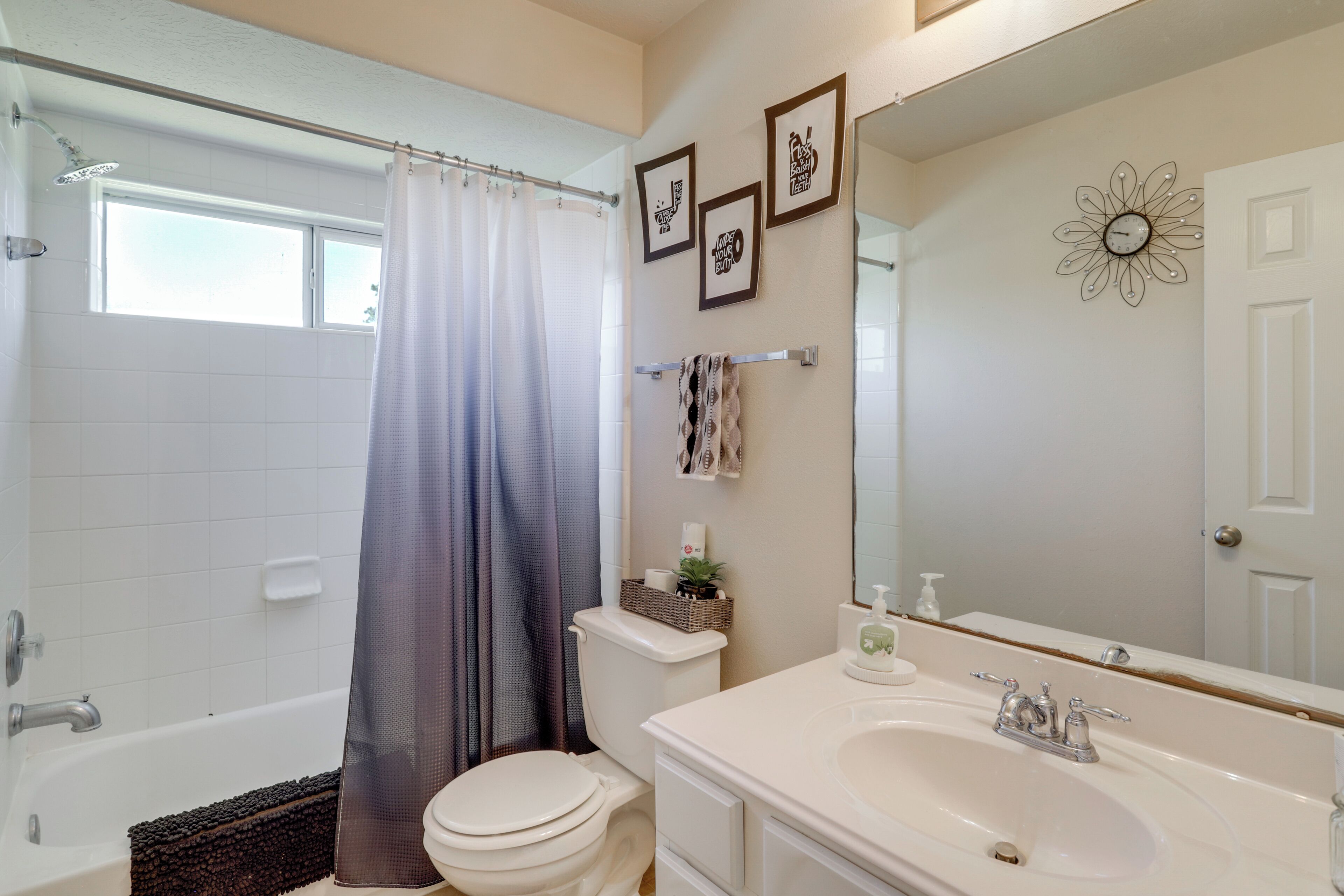 A bathroom with a bathtub, toilet, and sink. There are framed pictures on the wall and a shower curtain.