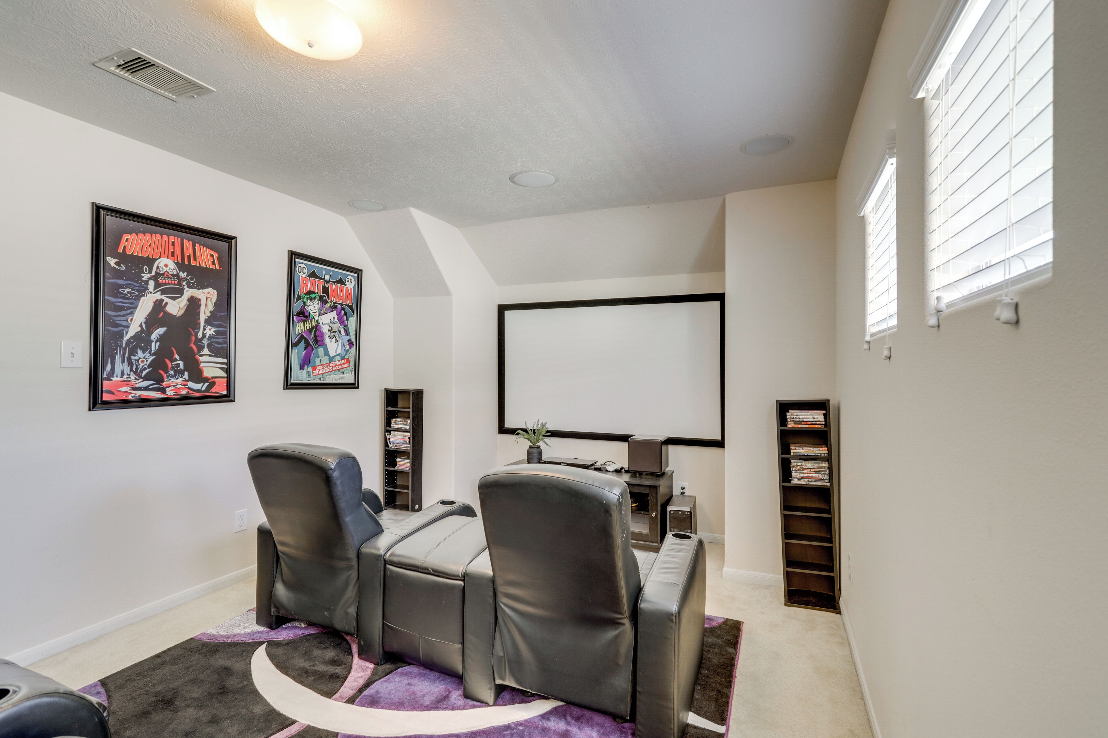 A home theater room with a large screen, leather recliner chairs, and framed posters on the wall.