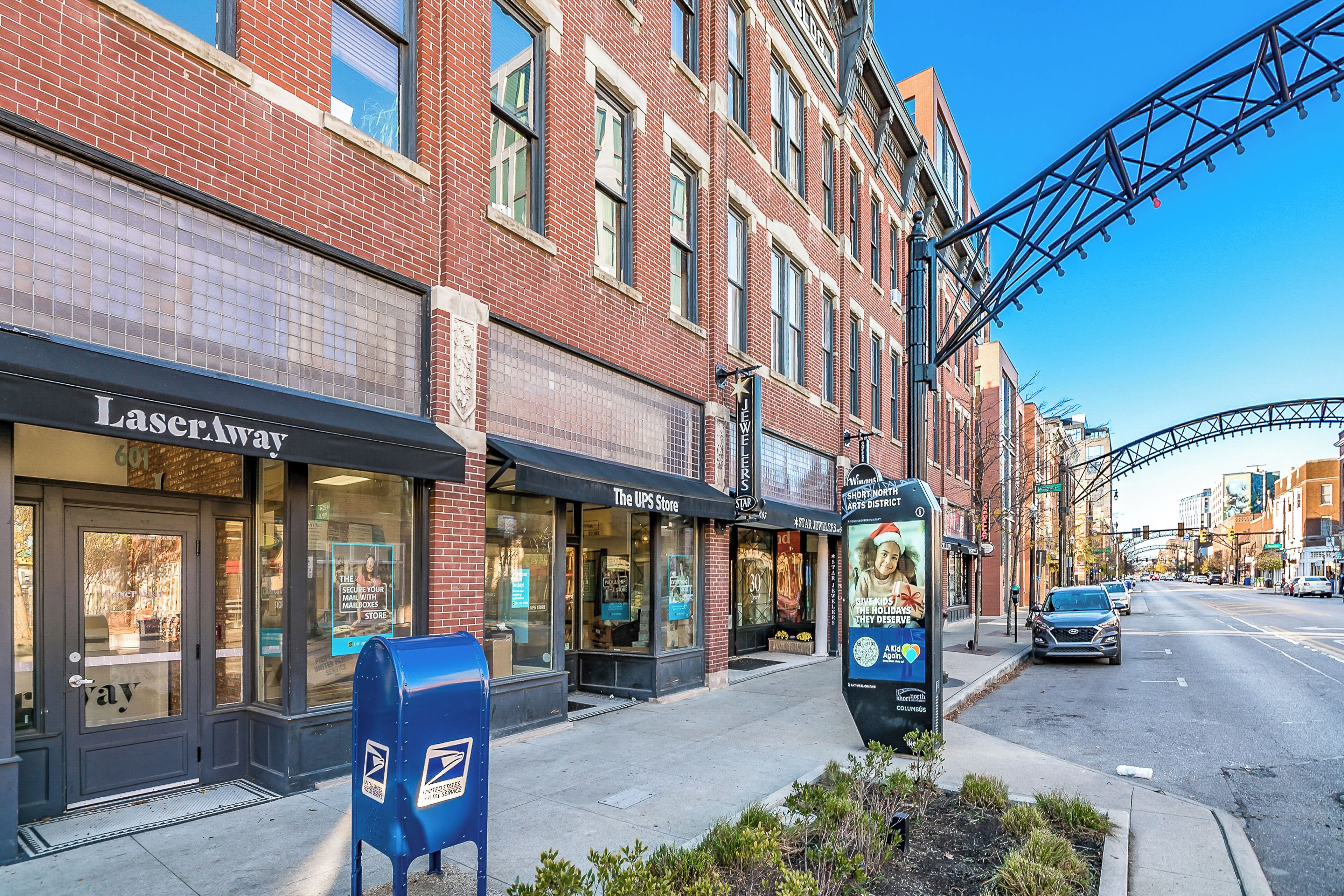 A street view with a UPS store, a LaserAway store, and a USPS mailbox.