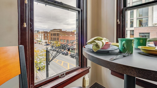 A window with a view of a street and buildings, a table with a plate, a green mug, and a fork. - Parking, Walk to Convention Center, Secured Entry (Columbus)