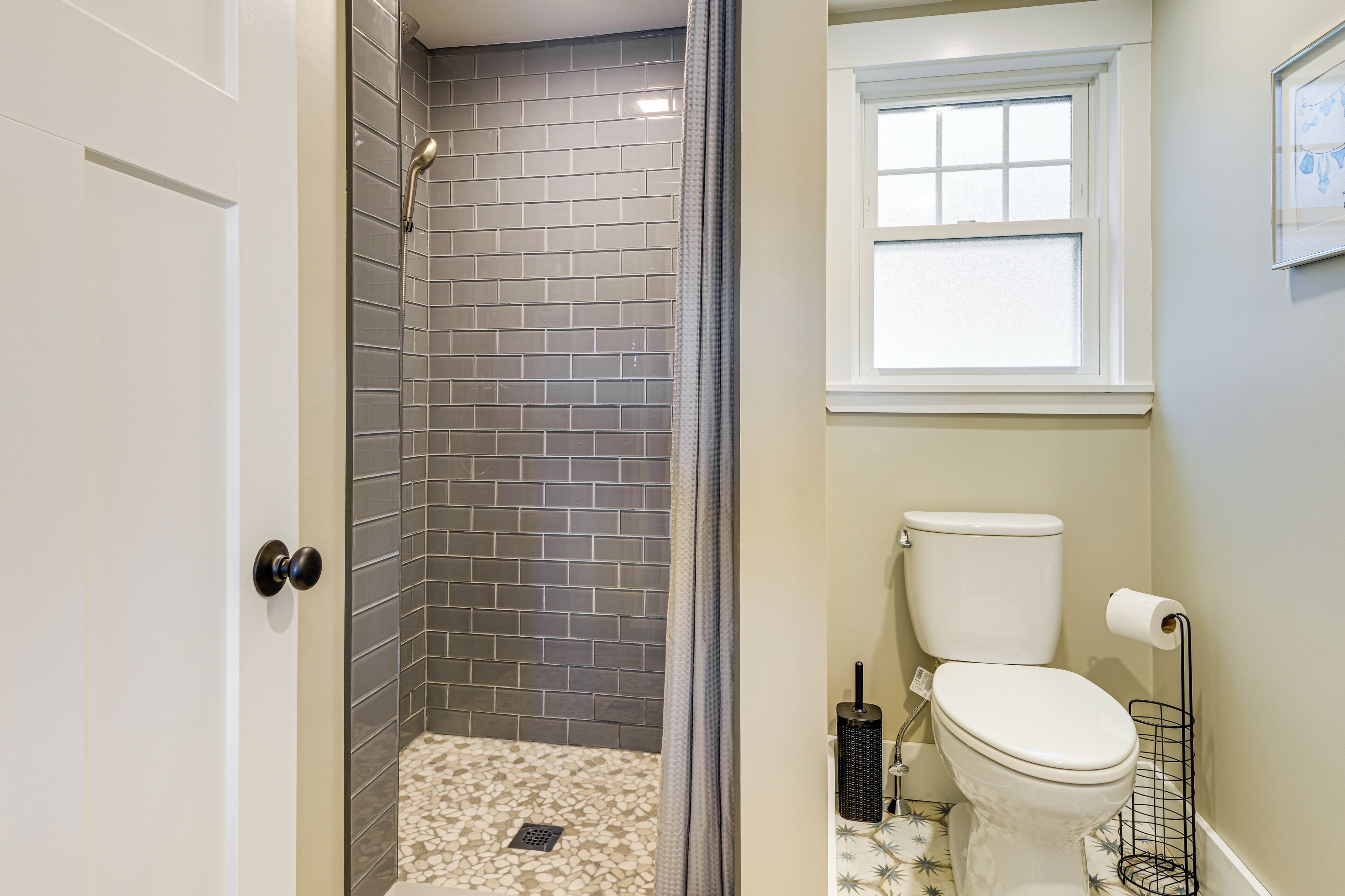 A bathroom with a shower area, toilet, and a window.