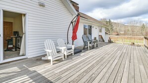 Une terrasse en bois avec des fauteuils Adirondack et un parasol rouge, une porte-fenêtre coulissante et une petite table d’extérieur.