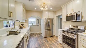 A modern kitchen with stainless steel appliances, white cabinetry, and a wooden floor.