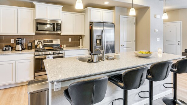 A modern kitchen with white cabinets, stainless steel appliances, a granite countertop, and black bar stools. - 10 Mi to Fort Carson: Newly Built Townhome! (Colorado Springs)