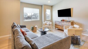 A modern living room with a sectional sofa, a coffee table, and a flat-screen TV mounted on the wall. - 10 Mi to Fort Carson: Newly Built Townhome! (Colorado Springs)
