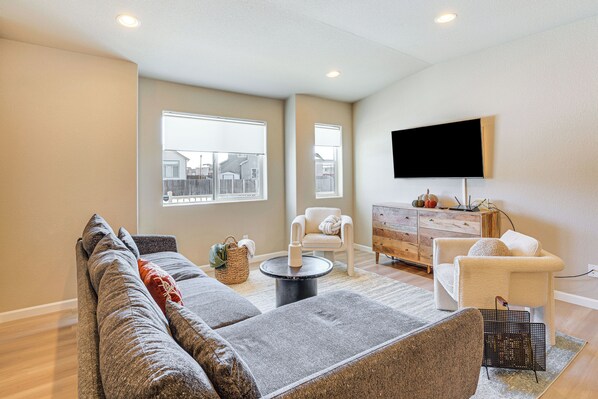 A modern living room with a sectional sofa, a coffee table, and a flat-screen TV mounted on the wall. - 10 Mi to Fort Carson: Newly Built Townhome! (Colorado Springs)