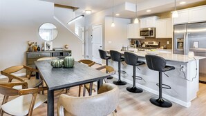 A modern kitchen with a central island, bar stools, and a dining area with chairs. - 10 Mi to Fort Carson: Newly Built Townhome! (Colorado Springs)