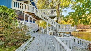 A wooden deck with a staircase leading to a second-story balcony overlooking a body of water.