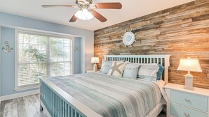 Ein Schlafzimmer mit Holzwand, einem Bett mit Kissen in Form eines Seesterns, einem Deckenventilator und einem Fenster mit Jalousien.