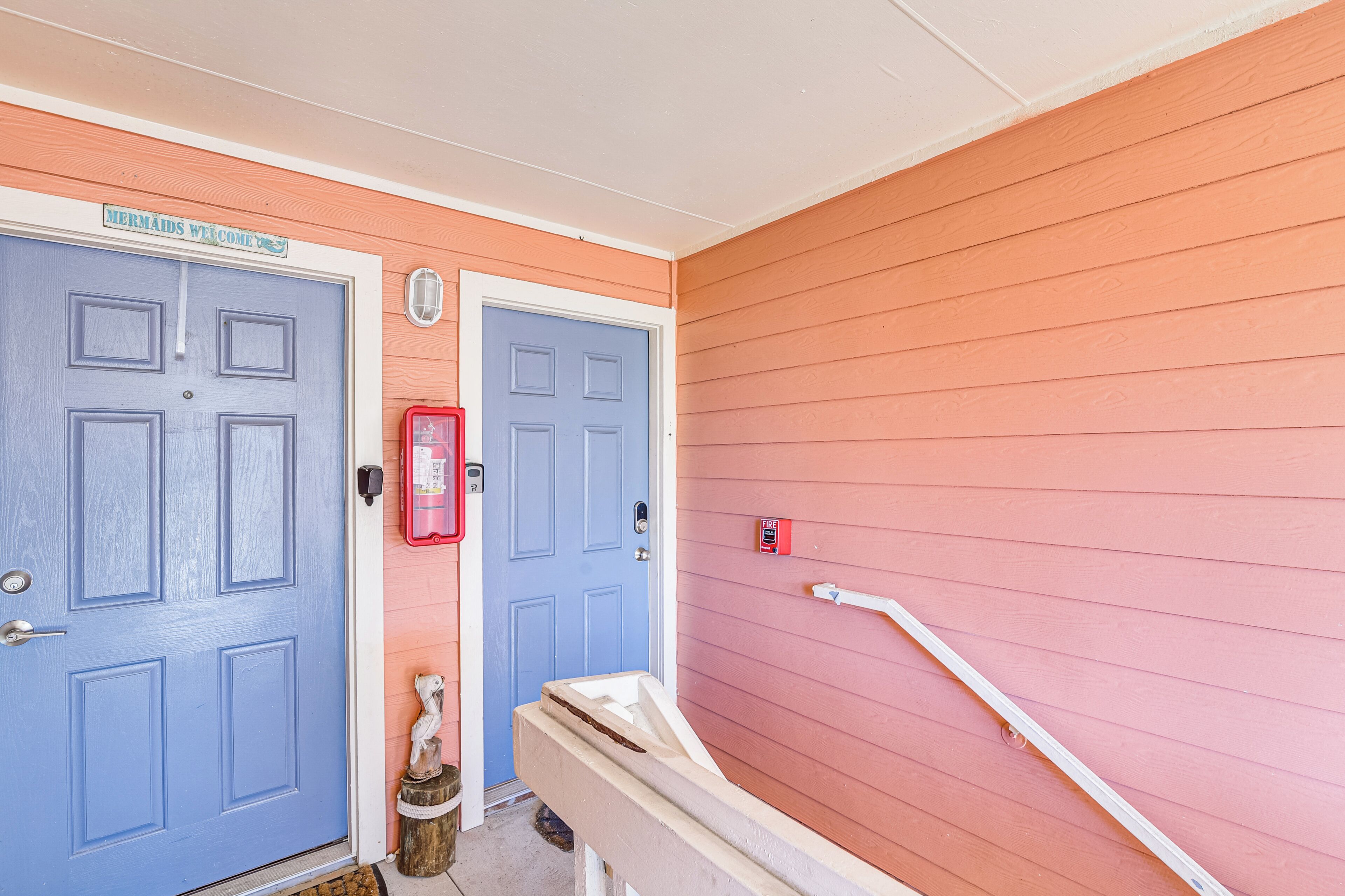 A house with two blue doors, one with a 'Mermaids Welcome' sign, and a red mailbox.