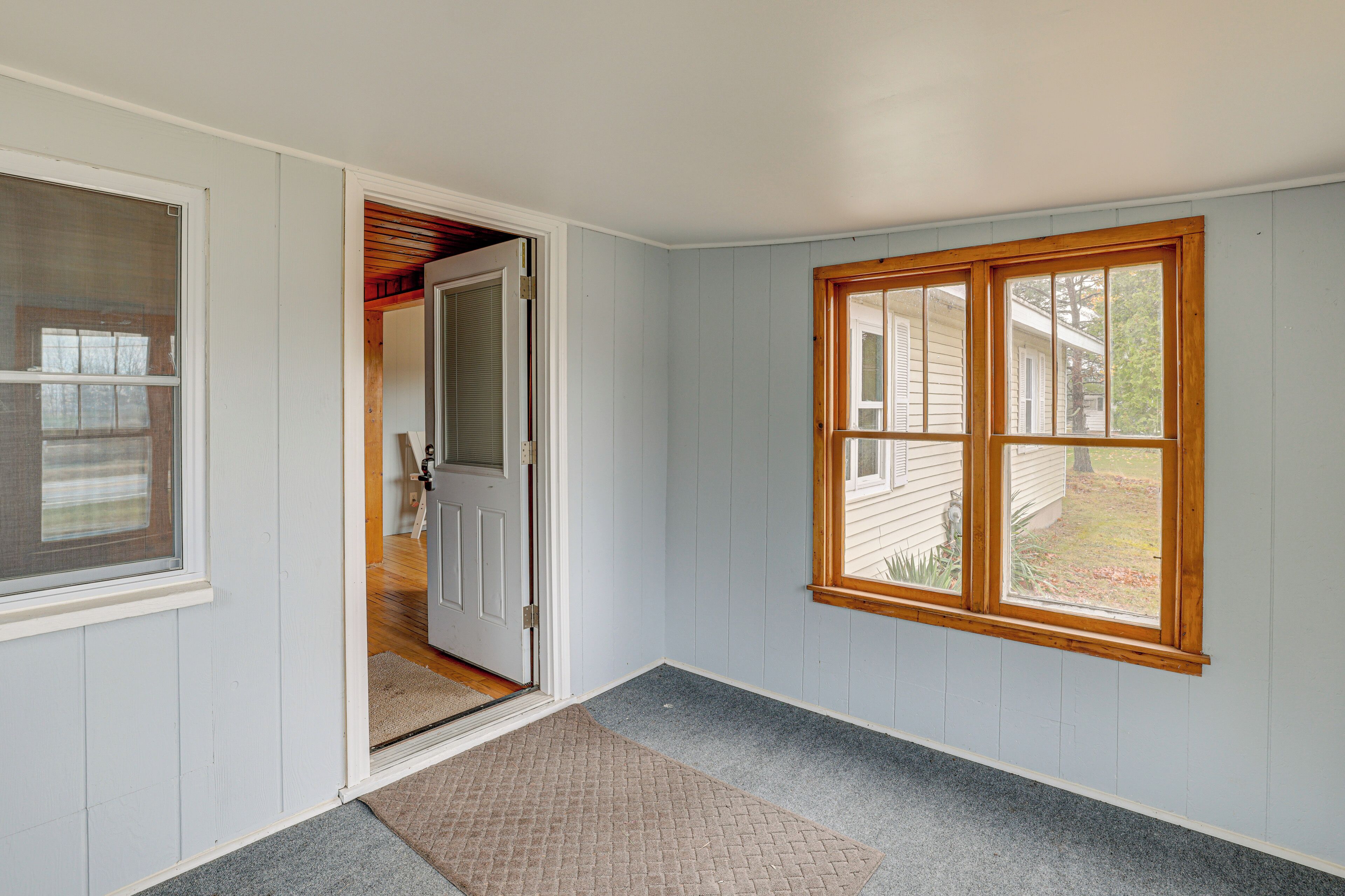 A hallway with a wooden-framed window, a door leading to another room, and a carpeted floor.
