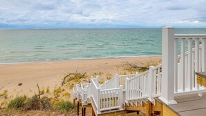 Une terrasse en bois, agrémentée de balustrades blanches, surplombe une plage et offre une vue sur l’océan.