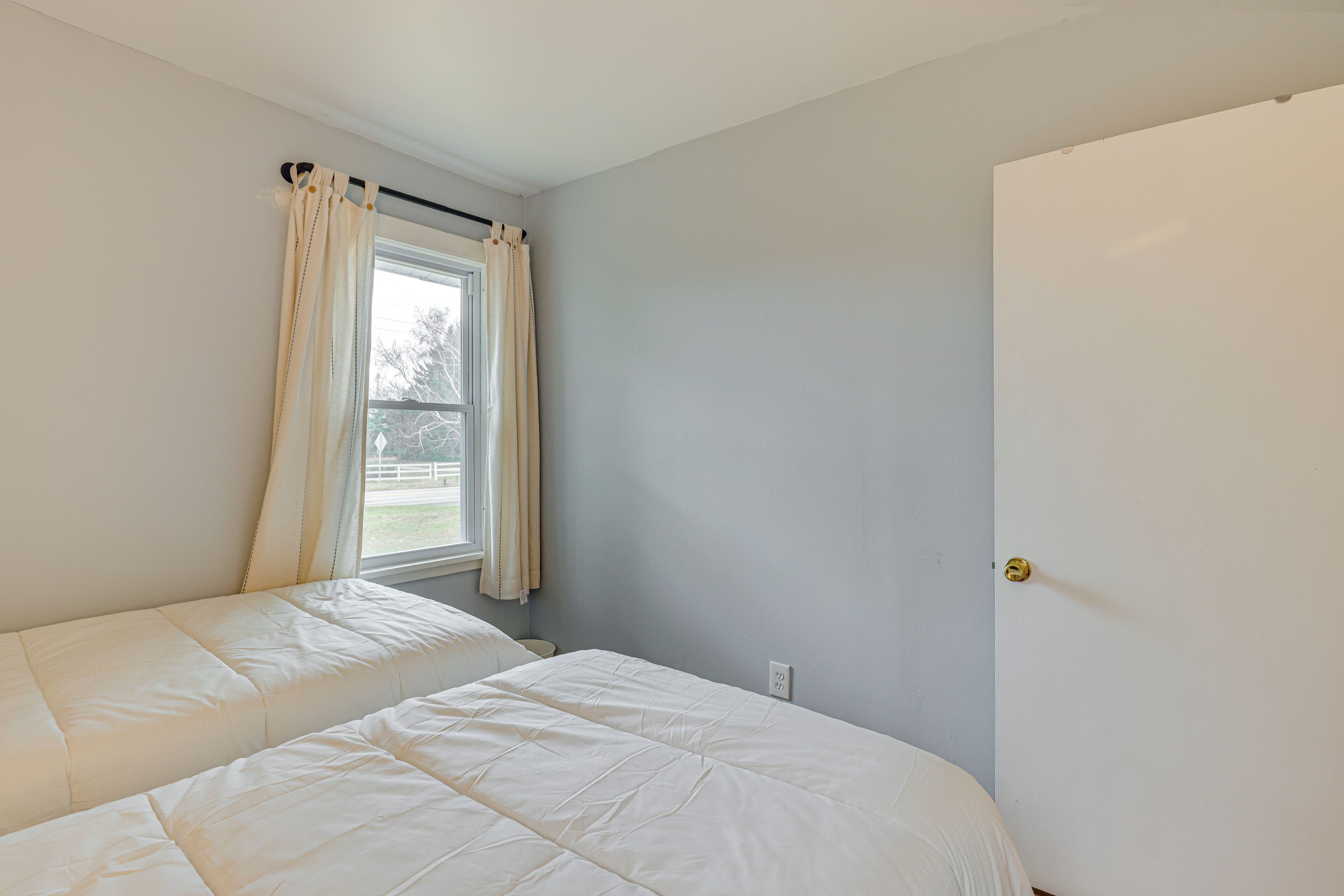 Quarto com duas camas, janela com cortinas e porta.