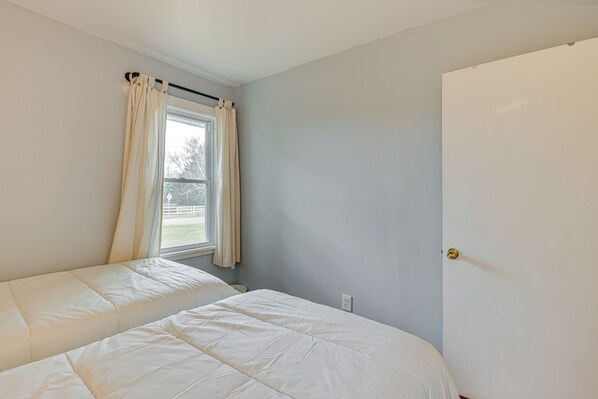 A bedroom with two beds, a window with curtains, and a door. - Walk to Beach & Lake Michigan: Manistee Bliss! (Manistee)