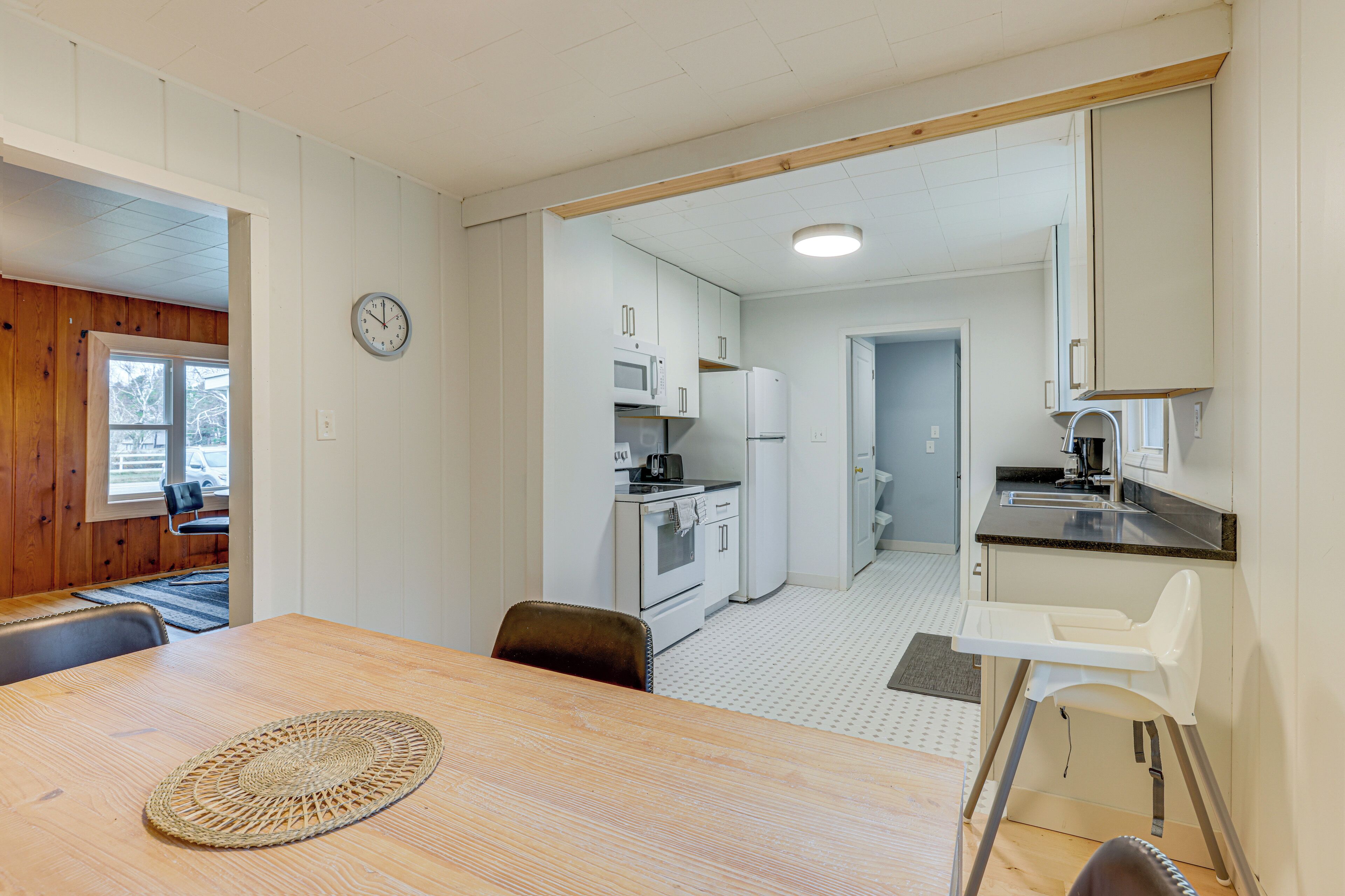 A compact kitchen with white appliances, a dining area with a wooden table, and a high chair.