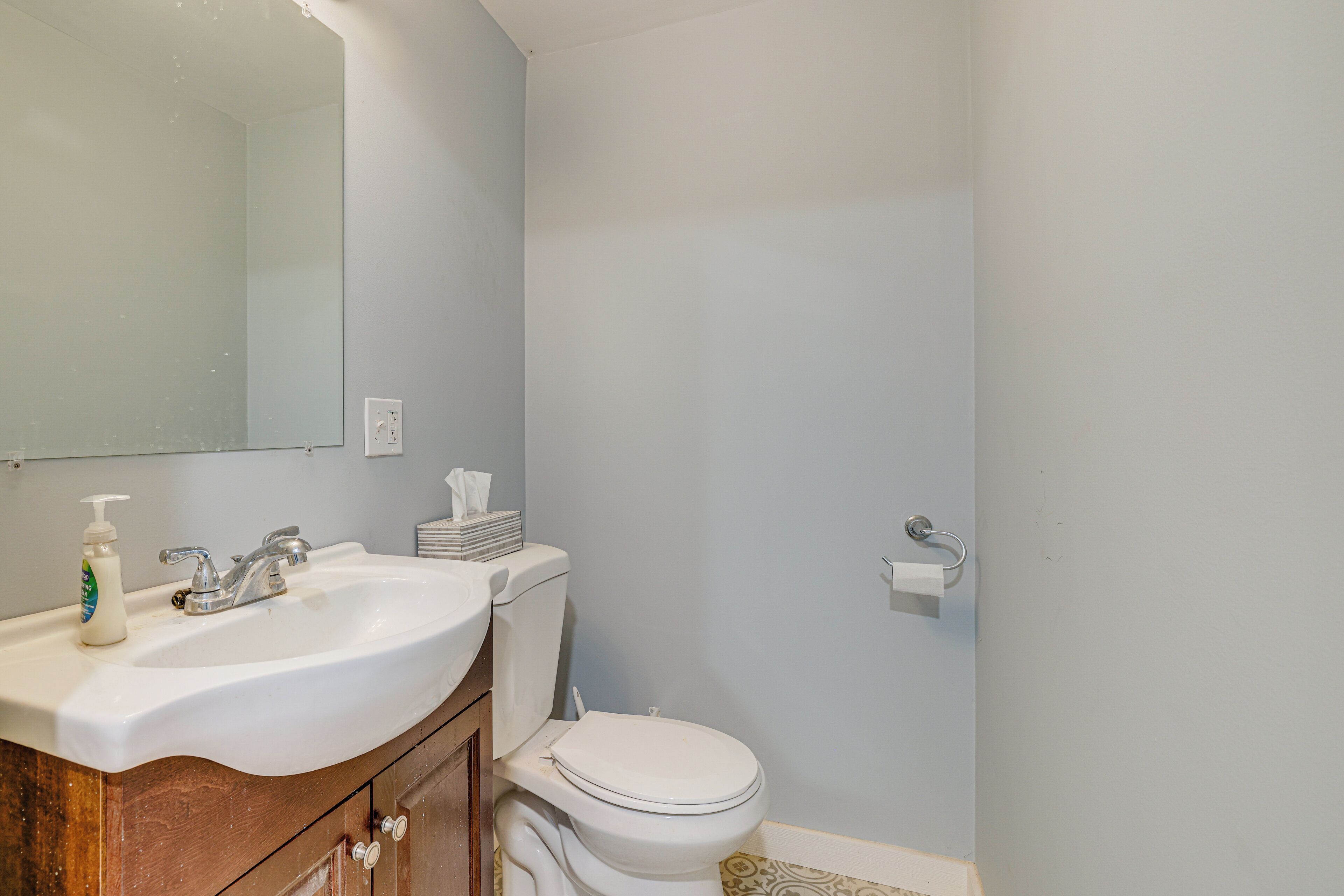 Un baño con lavamanos blanco, espejo, inodoro y toallero.