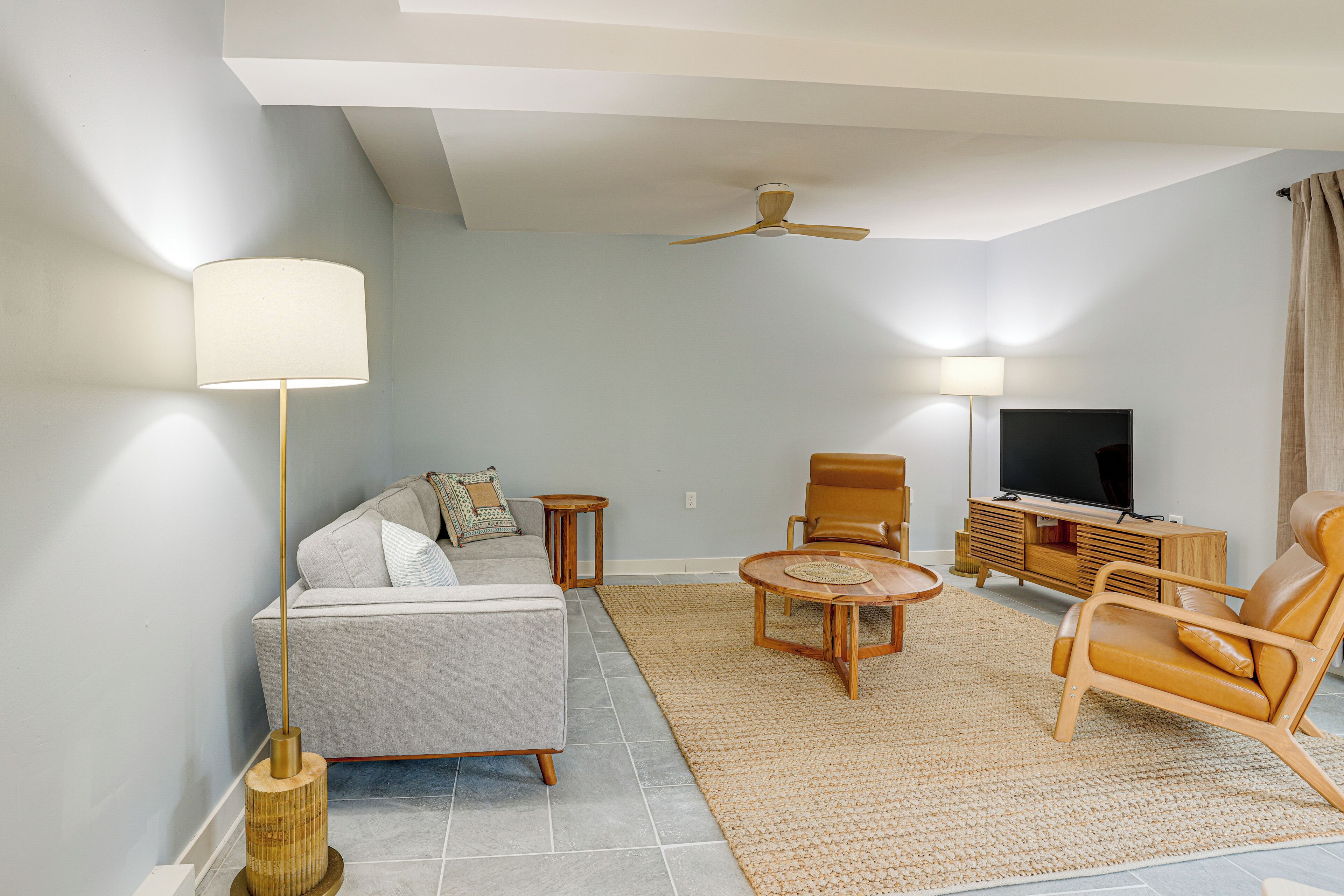 A modern living room with a sofa, two chairs, a TV, and a ceiling fan.
