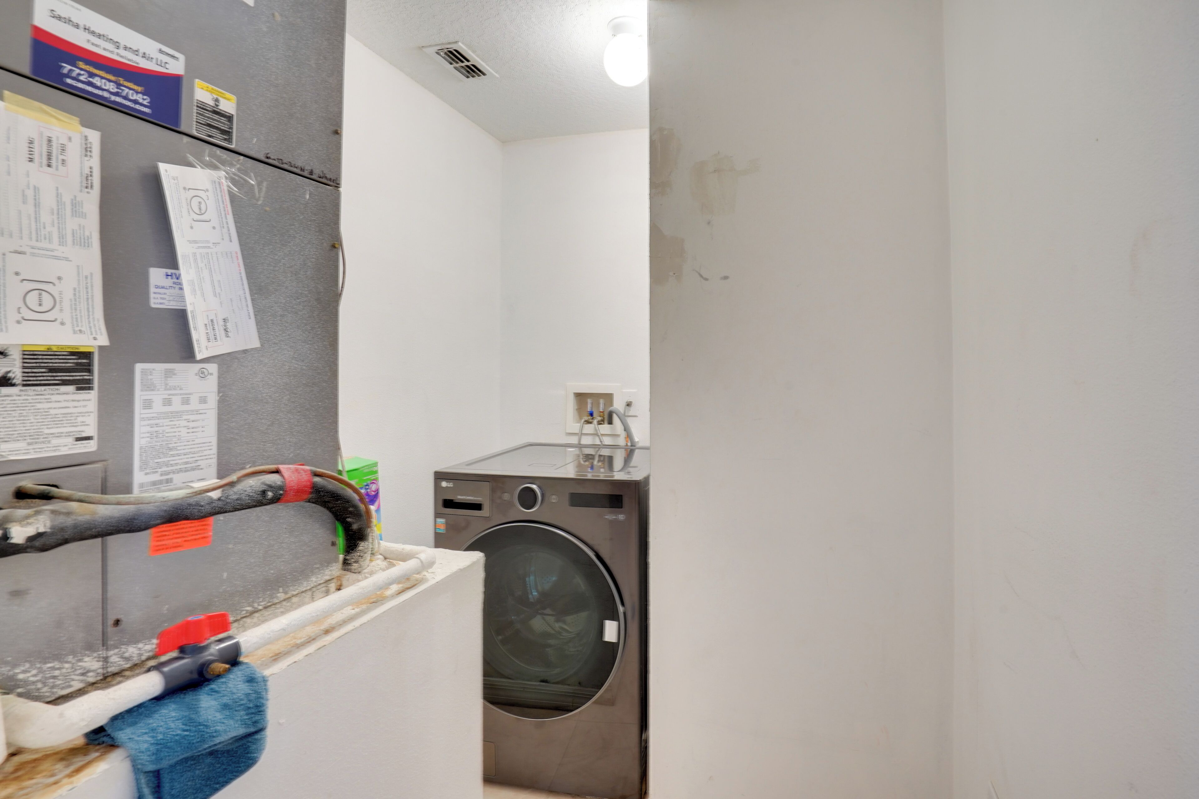 A laundry area with a washing machine, a utility meter, and various notices on the wall.