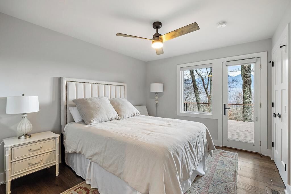 Ein Schlafzimmer mit Bett, Nachttisch, Lampe, Deckenventilator und Blick durch eine Tür.