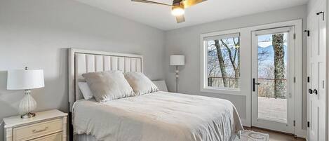 Ein Schlafzimmer mit Bett, Nachttisch, Lampe, Deckenventilator und Blick durch eine Tür.