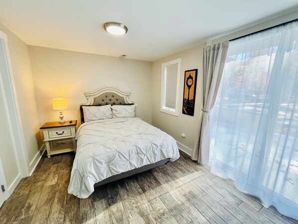 Une chambre à coucher avec un lit, une table de chevet, une lampe, une horloge et une fenêtre avec des rideaux.