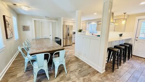 Una cocina amplia con una isla central, muebles blancos y una zona de comedor con sillas azul claro.